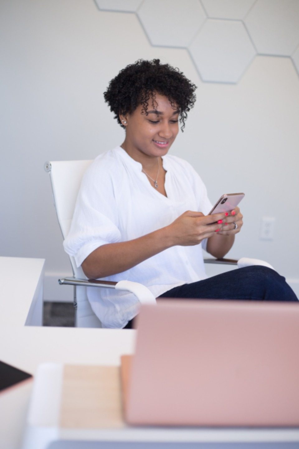 A woman in a white shirt reading her phone at a desk